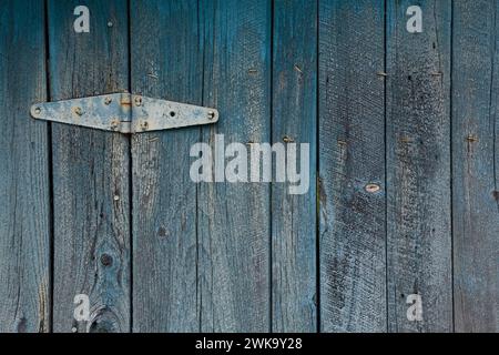 Close-up of metal hinge on wooden planks with faded and peeling teal blue paint. Stock Photo