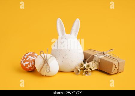 Decorated Easter eggs, bunny figure and present on yellow background Stock Photo
