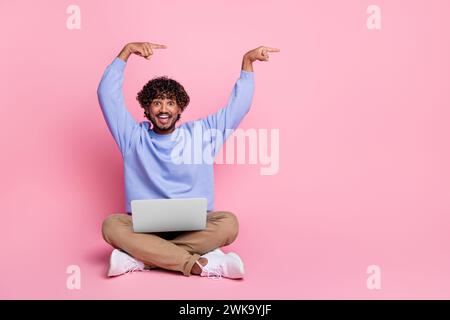 Photo of cheerful satisfied african man sit floor recommend buy credit modern gadget notebook empty space isolated on pink color background Stock Photo