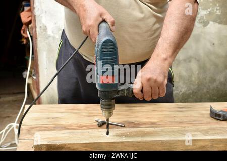The carpenter makes a hole with a drill in the board. Stock Photo