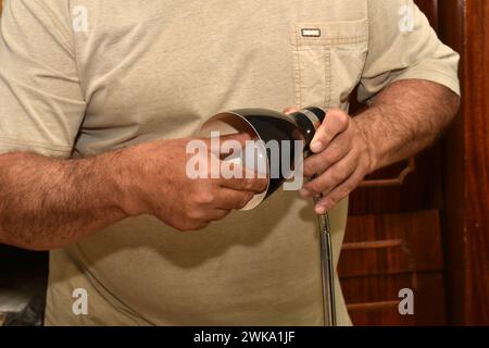 The picture shows a close-up of male hands, in one of them he holds a table lamp, and the other unscrews a burned-out electric light bulb from it. Stock Photo