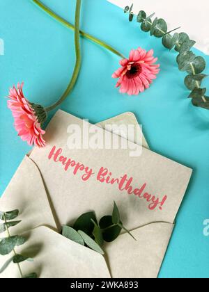 A pink envelope with a green birthday card placed inside, with pink gerbera flowers on white table Stock Photo