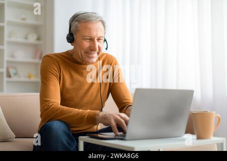Happy senior man with headset using laptop at home Stock Photo