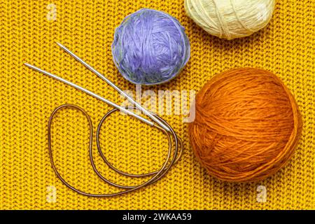 knitting needles and wool threads on a knitted background. knitting a sweater from wool threads Stock Photo