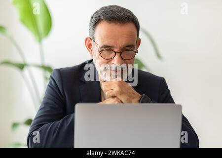 Focused senior businessman wearing glasses and a smart suit, deeply engrossed in his laptop Stock Photo
