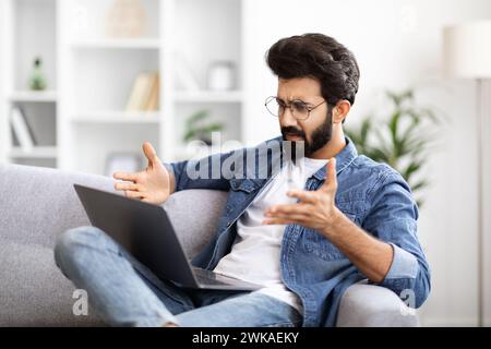 Confused Young Indian Guy Suffering Problems While Using Laptop At Home Stock Photo