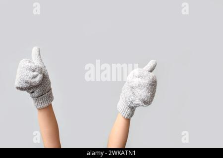 Hands in warm mittens showing thumbs-up on grey background Stock Photo