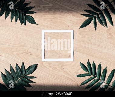 Layout with blank white paper frame and green leaves on wooden background. Creative natural background with copy space. Stock Photo