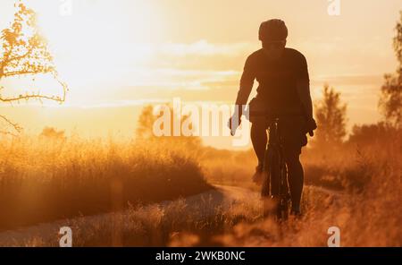 Silhouette of a cyclist on a gravel bike riding a countryside trail at sunset. Stock Photo
