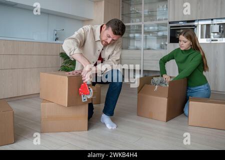 Focused man using tape packing cardboard boxes prepare to move with loving woman in new apartment Stock Photo