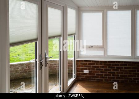Made to measure blinds on windows and doors in a white conservatory with wooden floor and red brick walls on a sunny day. The roof is an insulated war Stock Photo