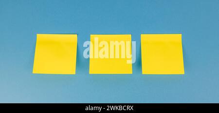 Three yellow blank square stickers on a blue background with copy space. Reminder and combination concept - close-up. Stock Photo