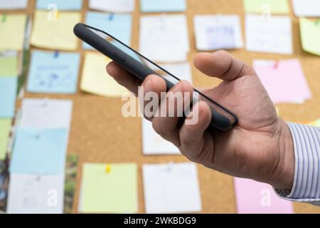 planning tasks and calendar events Using a smartphone. digital technologies to change a business model. Sticky notes on a cork board in the background Stock Photo