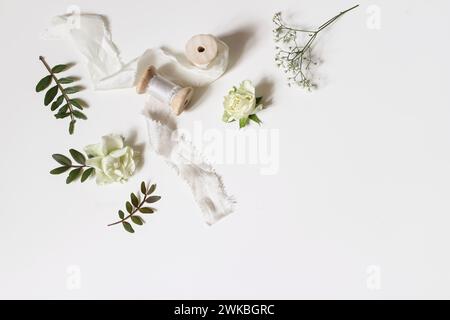 Floral wedding, birthday table composition. Gypsophila, rose flowers, green lentisk leaves and silk ribbons with wooden spools isolated on white table Stock Photo