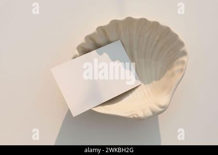Summer wedding stationery. Blank greeting, RSVP or business card mockup in sunlight. Invitation, template. Beige sea shell plate isolated on table Stock Photo
