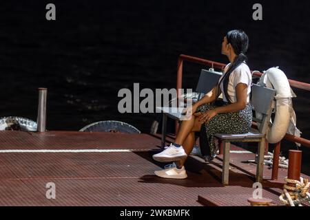 A young woman sits on an illuminated bench of a night ferry Stock Photo