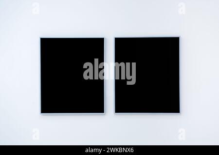 Mockup two blank space in black vertical square artist painting frames, isolated on white wall background. Empty 2 photo frames hanging on white wall Stock Photo