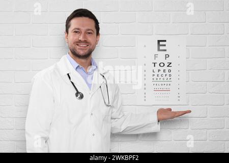 Ophthalmologist showing vision test chart on white brick wall Stock Photo