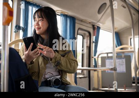 A happy Asian female solo traveler is checking a map on her smartphone while on the bus. public transportation concept Stock Photo