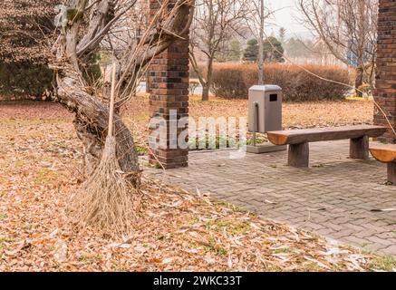 Old straw broom leaning against gnarly tree next to covered park benches in South Korea Stock Photo