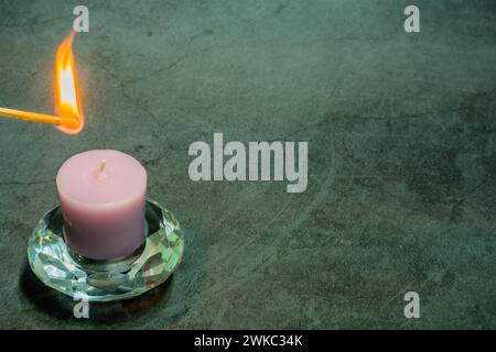 Lit matchstick over lavender candle in glass holder isolated on black textured background Stock Photo