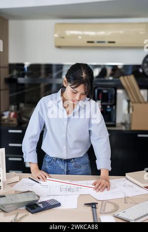 Asian architect engineer women working to designing new project about building model and construction architectural plan while using ruler to checking Stock Photo