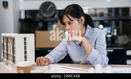 Asian architect engineer women working to examining design of architecture building model and taking notes in paper while planning construction and ar Stock Photo