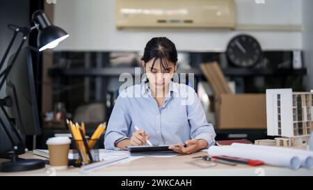 Asian architect engineer women working to checking about drawing architecture plan on digital tablet while creative to designing new project about bui Stock Photo