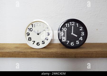 White and Black alram clock show time difference on wooden shelves Stock Photo