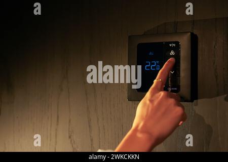 A persons hand is seen adjusting a digital smart thermostat to maintain a comfortable room temperature during the evening. Stock Photo