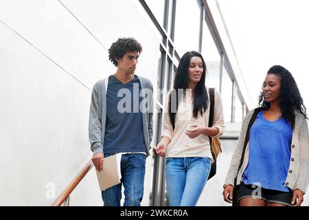 University, friends and group of students walking on stairs talking, speaking and in conversation on campus. Education, college and women and men chat Stock Photo