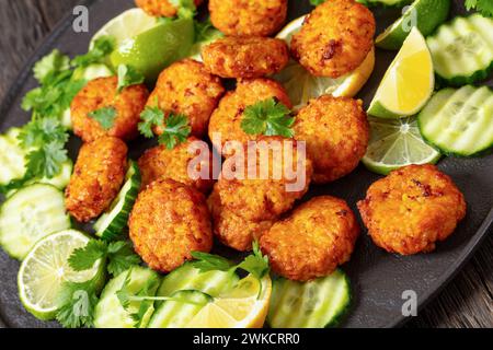 fried rice cutlets, rice tikki, indian style on black plate served with cucumber, lemon, lime slices and cilantro, close-up Stock Photo