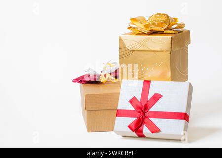 Three gift boxes wrapped in paper and tied with ribbon and bows on white background. Copy space. Front view. Red, white and golden colors Stock Photo