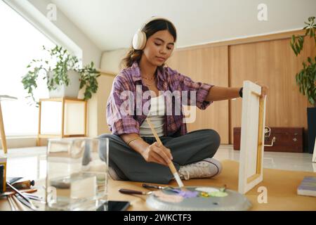 Teenage girl listening to music in headphone when painting on canvas Stock Photo