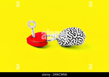Red heart-shaped padlock, complete with a tiny key, and a steel replica of the human brain set against a bold yellow backdrop. Intellect and sentiment Stock Photo