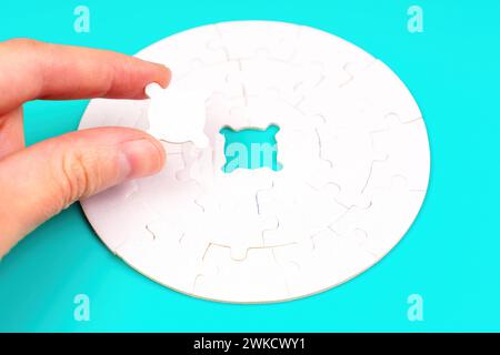 Hand delicately inserts the final piece into a circular puzzle. Completion, problem-solving and success related concept. Stock Photo