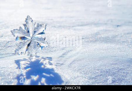 Winter background made from a large crystal snowflake ornament standing in the glittering snow casting a long shadow. Stock Photo