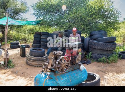 millennial african american workers ,working on the side of the road changing and fixing tires, air compressor in the foreground Stock Photo