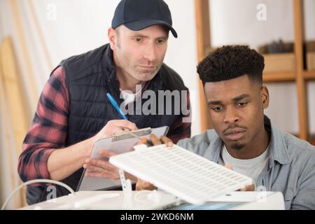 man assessing apprentice assembling an air-conditioning unit Stock Photo