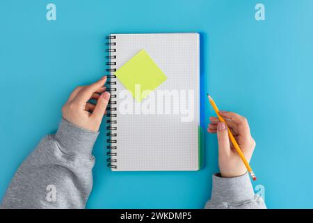 A woman student writes in a notepad on a blue background, top view. Stock Photo
