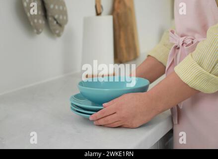 Woman putting plates on white marble countertop in kitchen, closeup view Stock Photo
