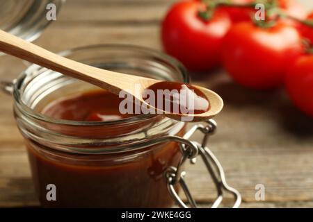 Tasty barbeque sauce in jar and spoon on table, closeup Stock Photo