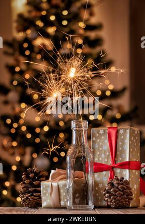 Burning sparklers in glass bottle with Christmas gifts on the background of blurred Christmas tree. Stock Photo