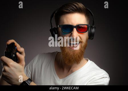 technology, gaming and people concept - angry young man or gamer in headphones with gamepad playing and streaming video game over grey background Stock Photo