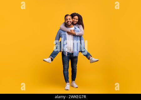 Romantic Young Black Man Piggybacking His Cheerful Girlfriend, Having Fun Together Stock Photo