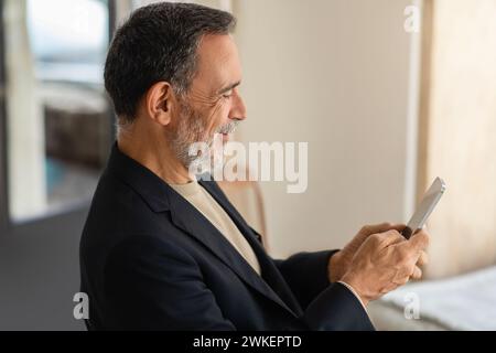 Profile view of a cheerful senior man in a smart casual outfit using a smartphone Stock Photo