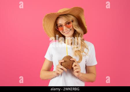 Joyful blonde traveler woman in hat with coconut cocktail, studio Stock Photo