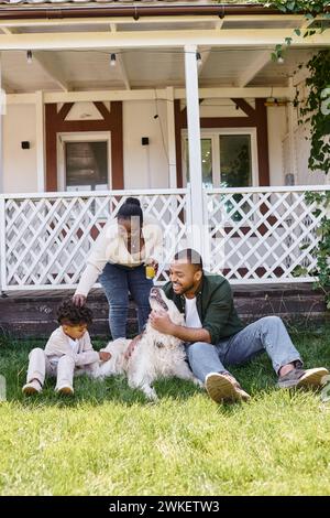 family time, happy african american parents and curly son playing with dog on backyard of house Stock Photo