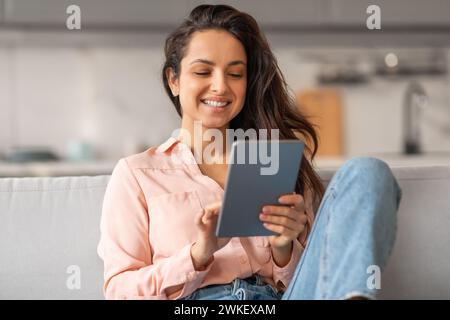 Happy woman using tablet on sofa at home Stock Photo