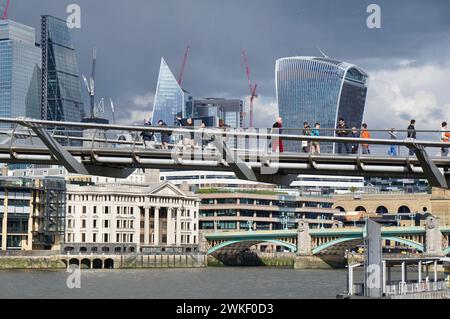 Millennium Bridge cutting through modern London skyline on a sunny day with a dramatic backdrop of stormy sky. Stock Photo
